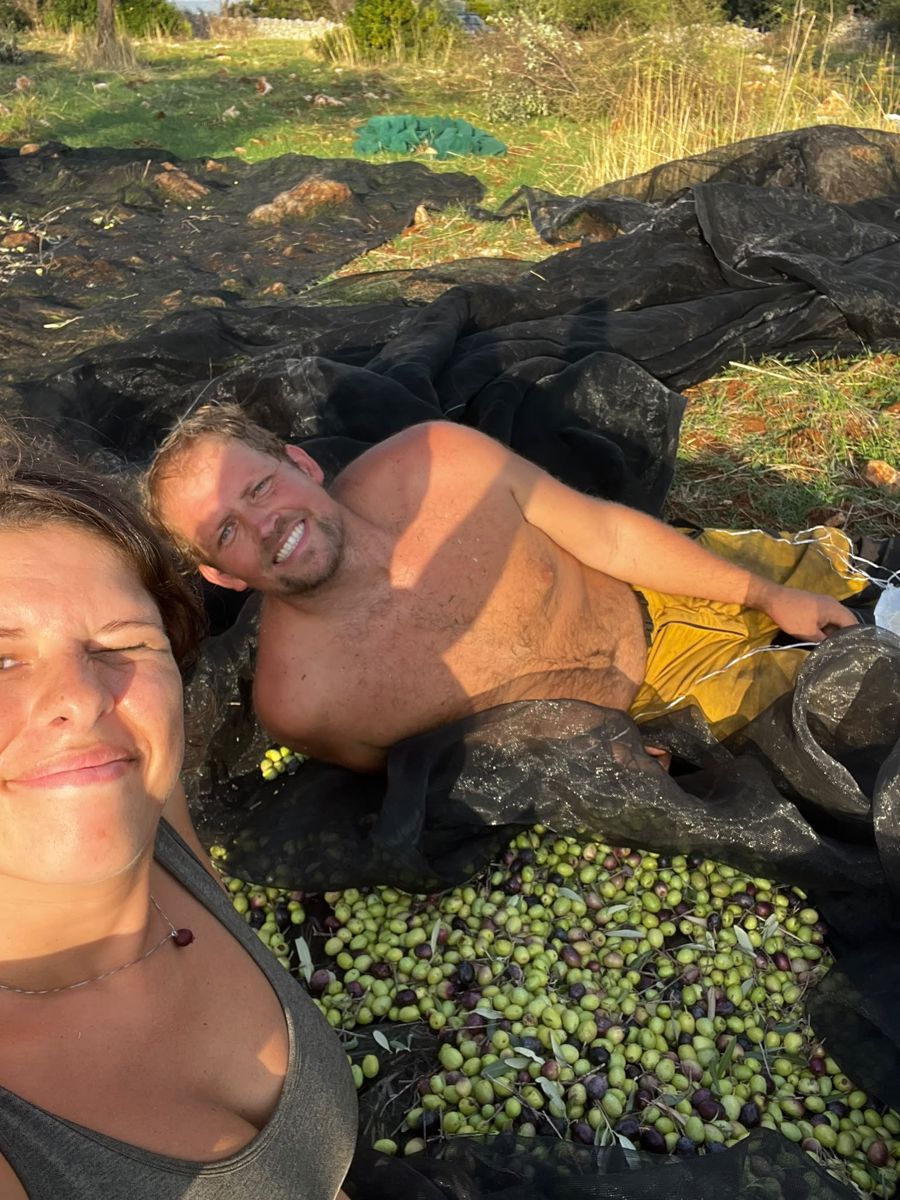 Bram ligt tussen de geoogste olijven, Maaike lacht in de camera